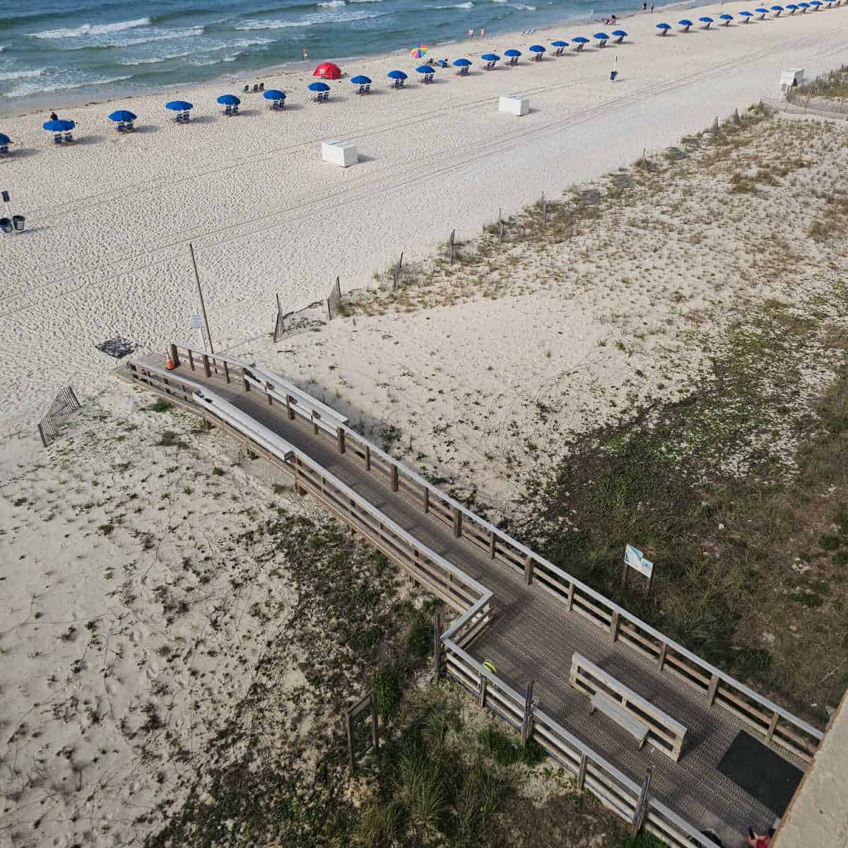 boardwalk over the sand leading to the beach with blue umbrellas lined up on the sand, Gulf waters in the corner
