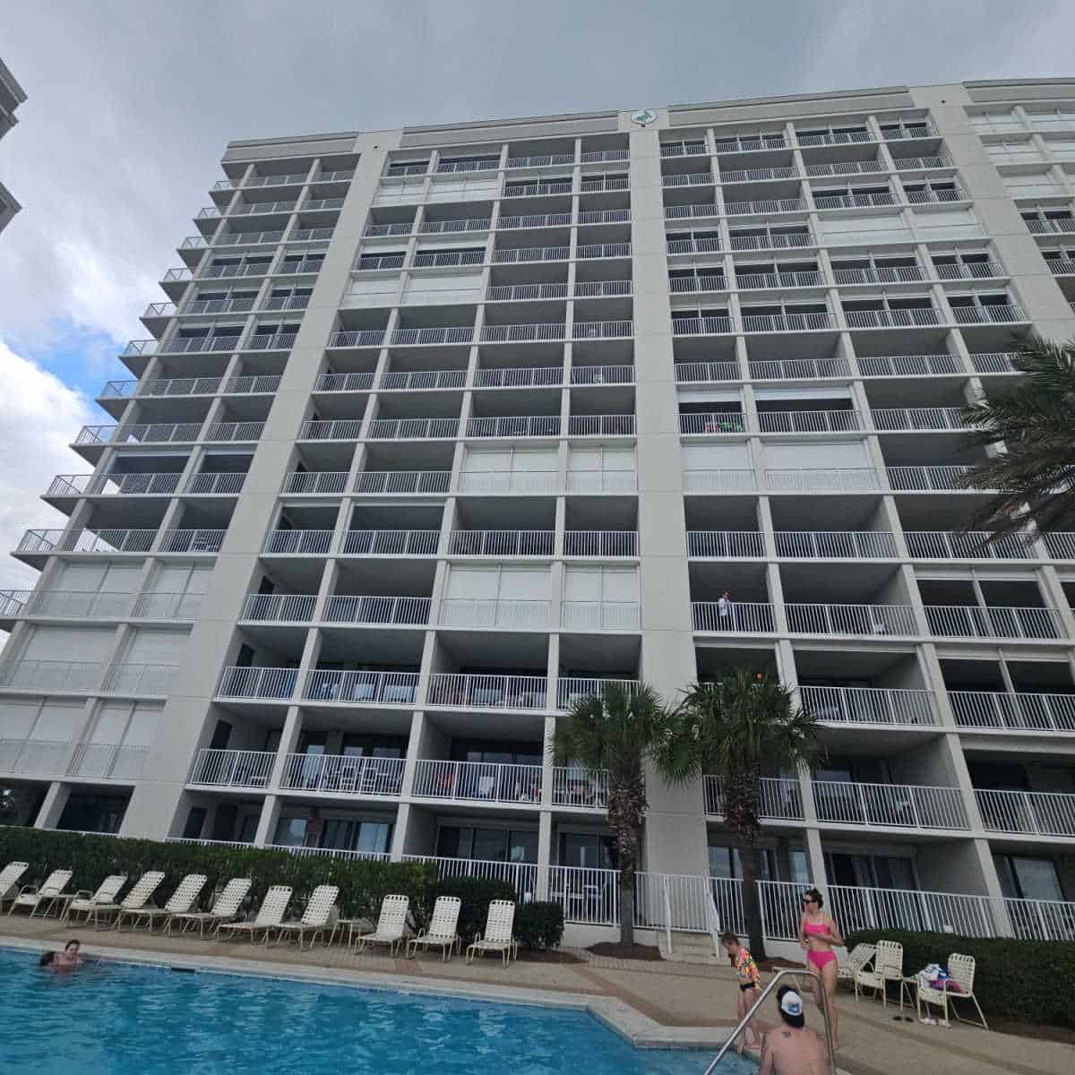 looking over the pool to a condo building exterior with a few palm trees