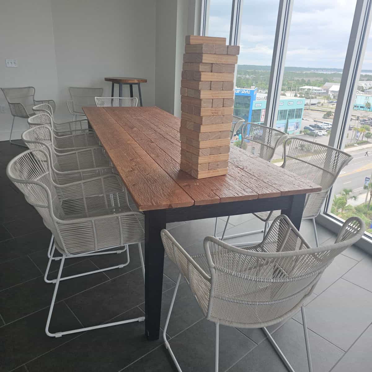 table with a large jenga game stacked on top of it, white chairs around the table, looking out the window to the Surf Style building in Gulf Shores from Gulf Place Condos