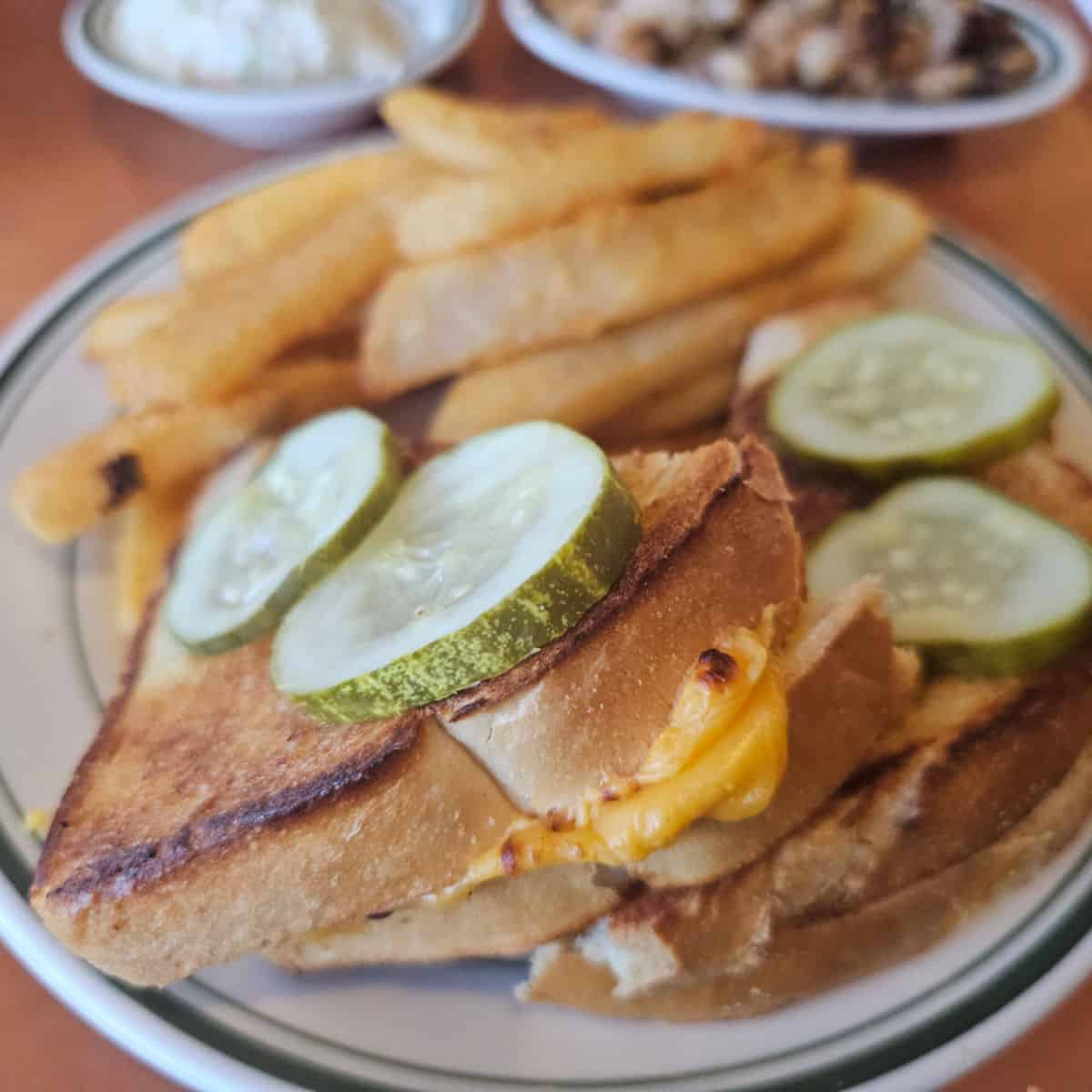 grilled cheese sandwiches with pickles on top next to french fries