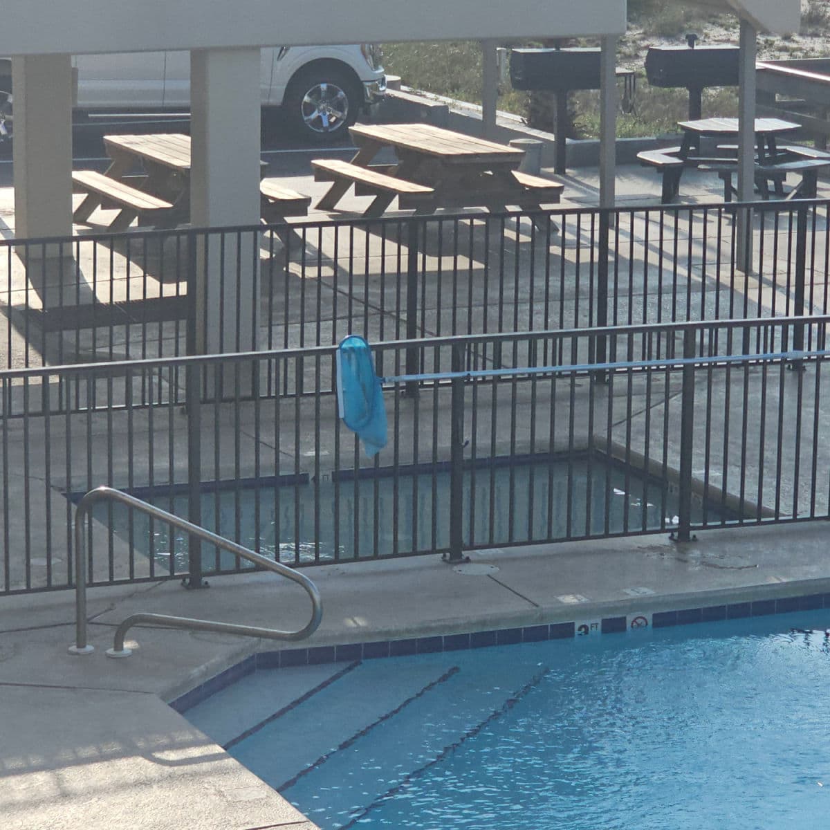 Small pool behind a fence, larger pool in front of a fence, picnic tables and bbq's behind the fence