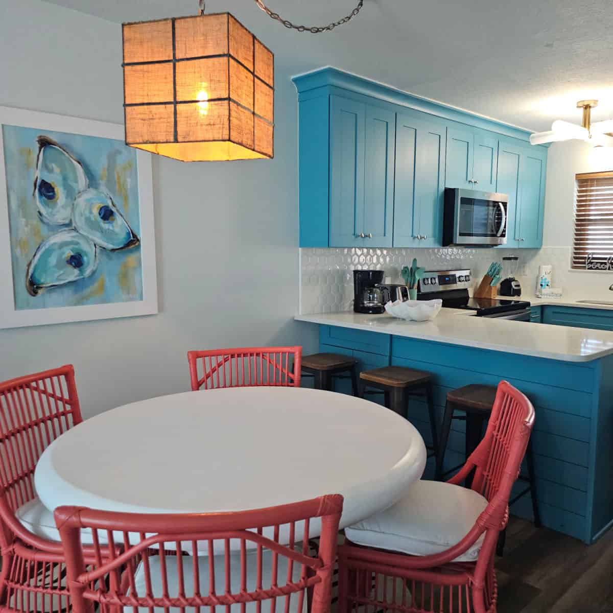 blue kitchen cabinets, oyster art on the wall over a white table with coral pink chairs.