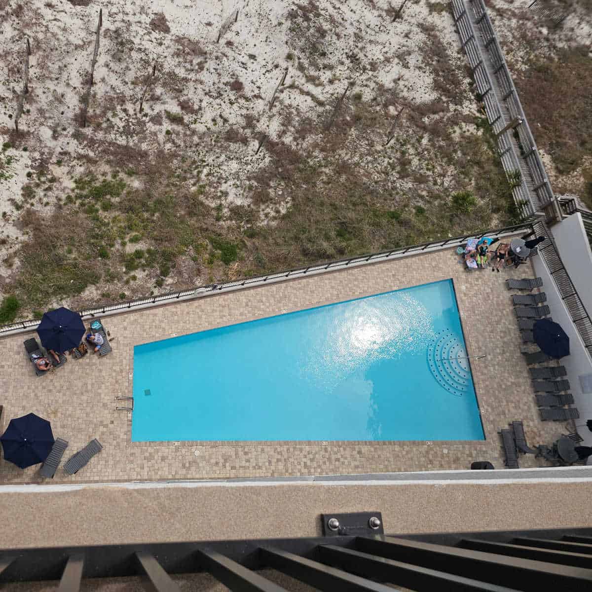 looking over an outdoor pool with pool chairs, boardwalk over the sand