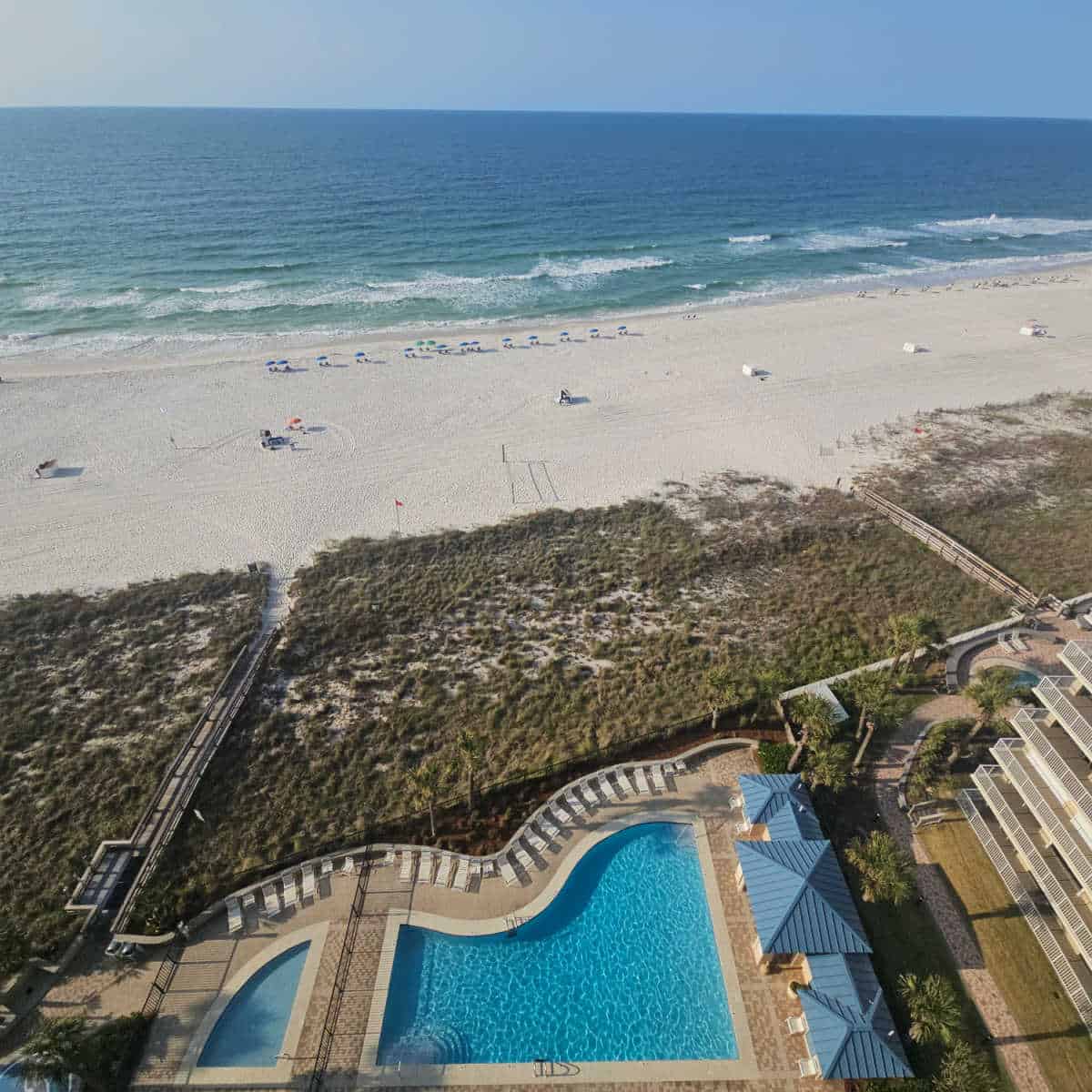 outdoor pool with chairs around the pool deck, sand dunes leading to the sand with Gulf waters in the background