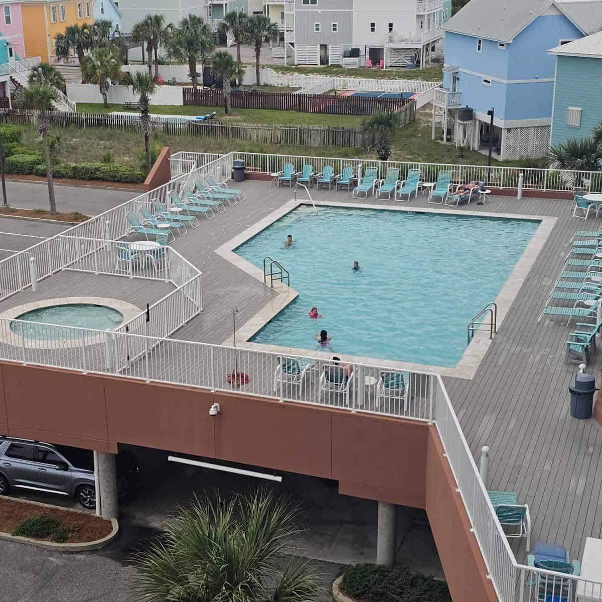pool and hot tub on a portico with lounge chairs around the deck, car parking under the pool deck