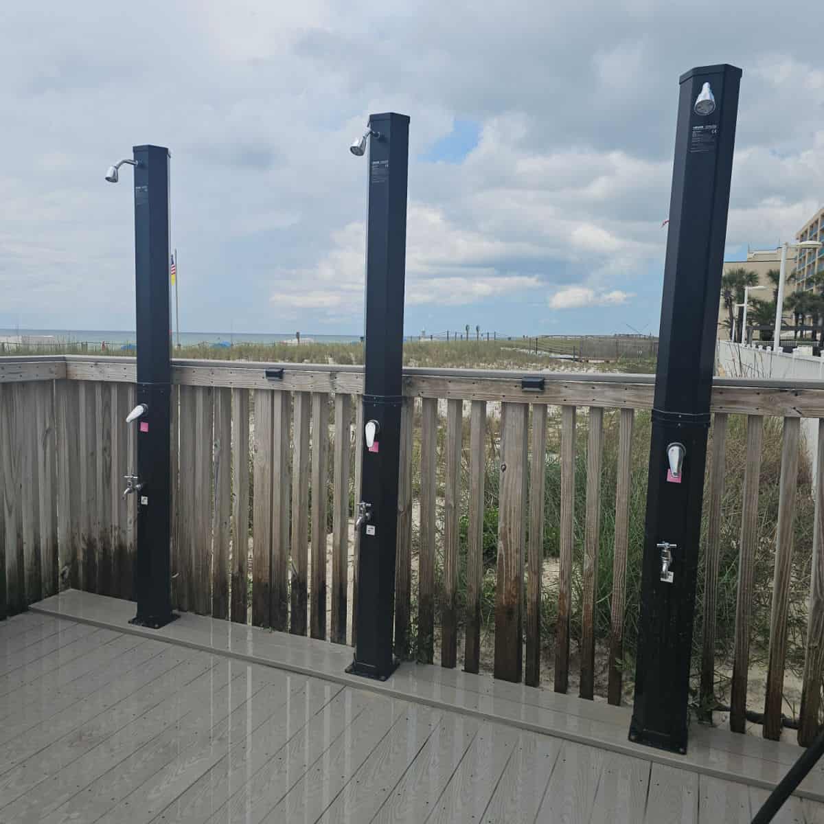 outdoor showers next to a wooden walkway, beach in the background