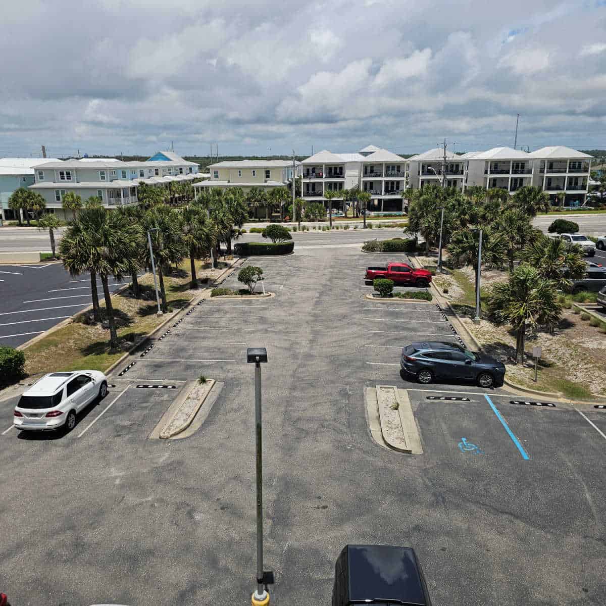 paved parking area with trees lining down the side, buildings across the street