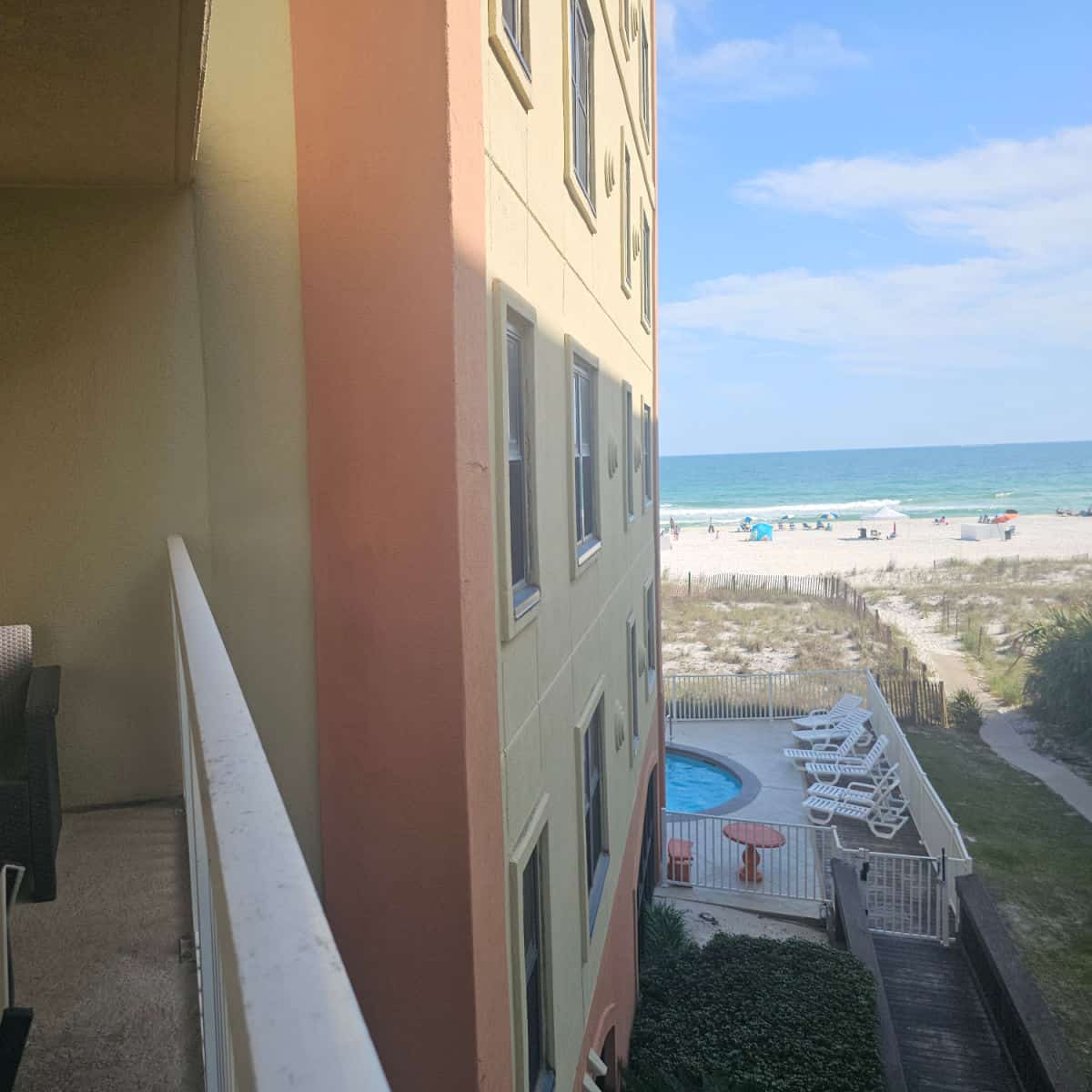 Looking down the side of Harbour Place from a balcony with the edge of the pool showing and then the Gulf of Mexico and white sand beach.