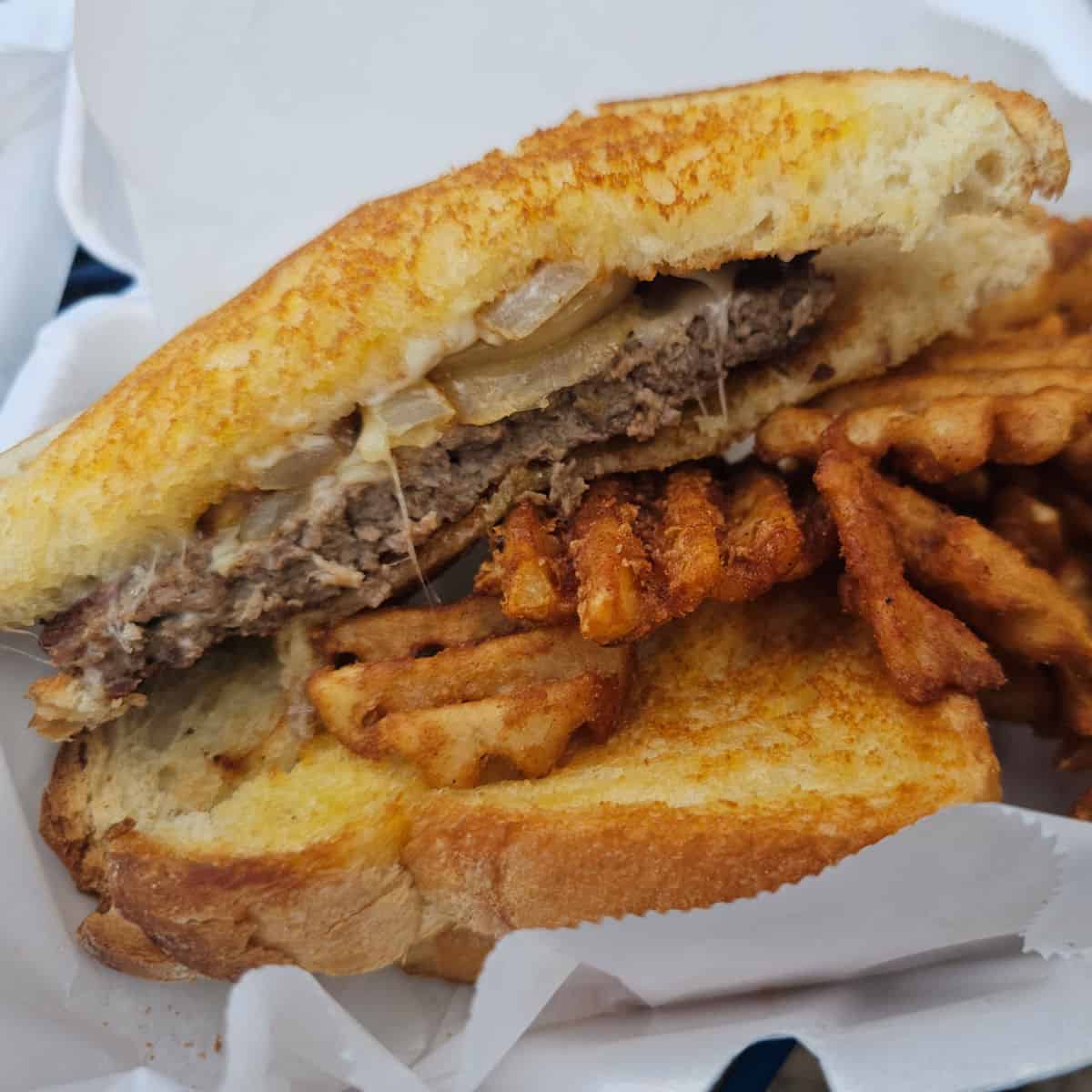 Patty melt with waffle fries in a white container