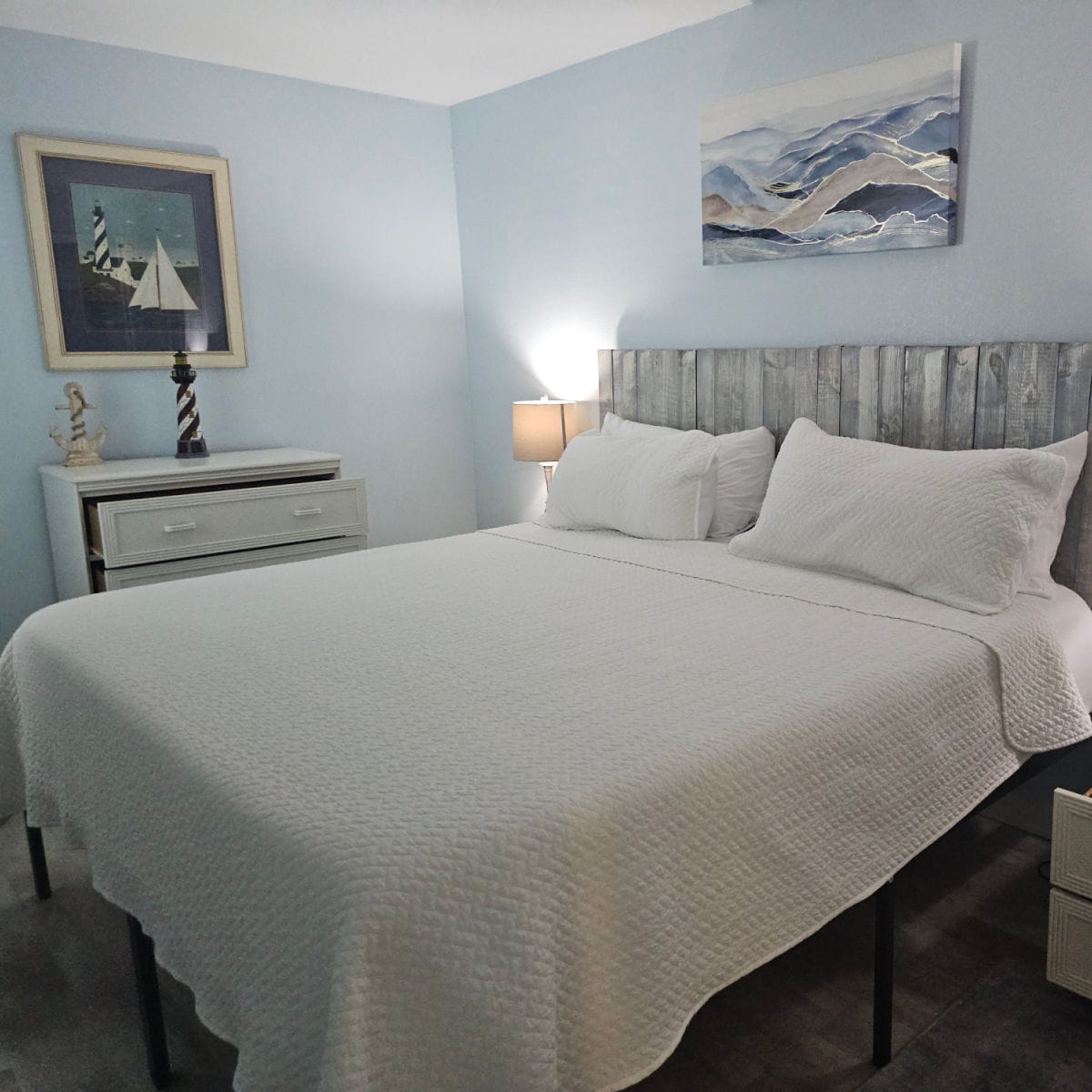 bedroom with white linens on the bed, art on the wall, white dresser in the corner