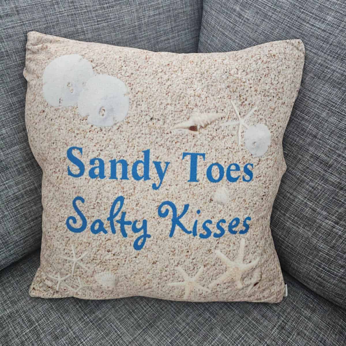Sandy Toes Salty Kisses pillow on a grey couch