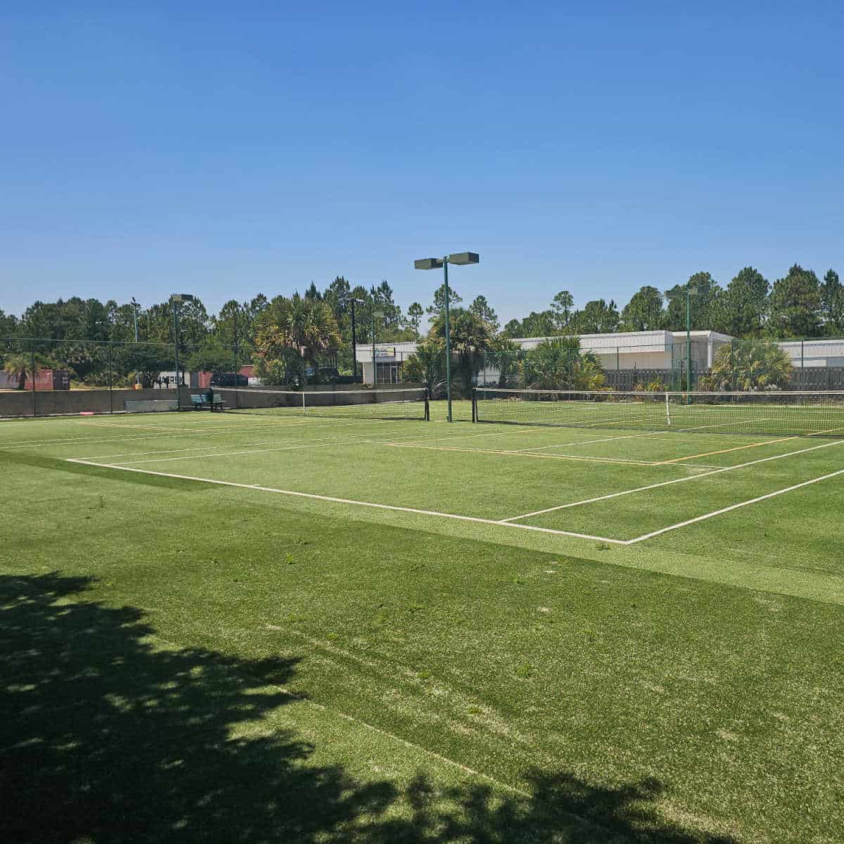 green grass tennis field outside with lights in between them