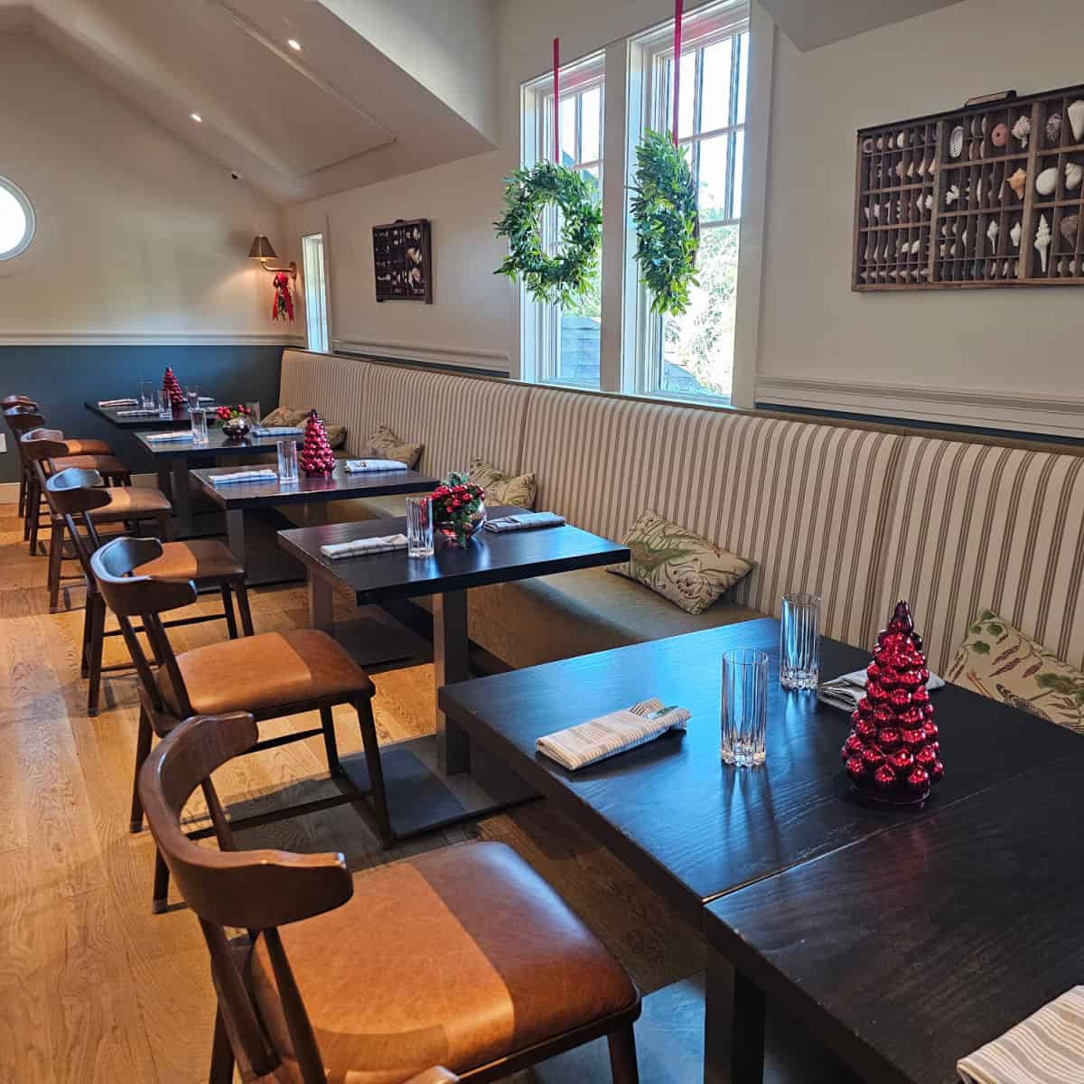 indoor seating areawith long padded bench, tables and chairs, shell decorations on the wall, wreaths hanging on the window