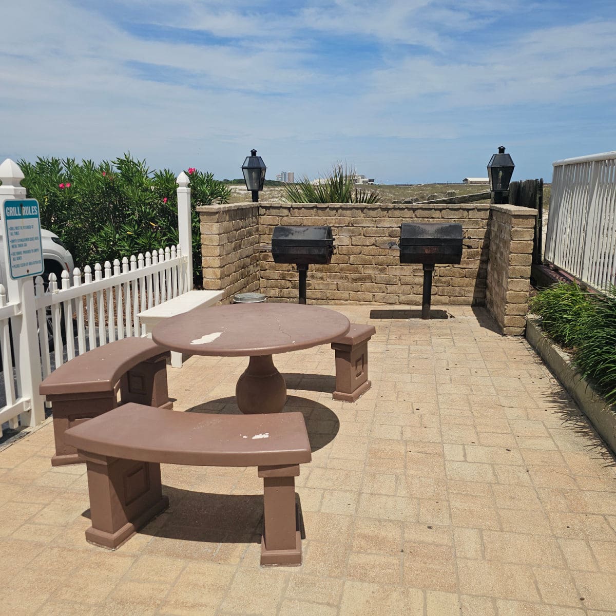 two charcoal barbecues near a brick fence, table with rounded benches and a white fence