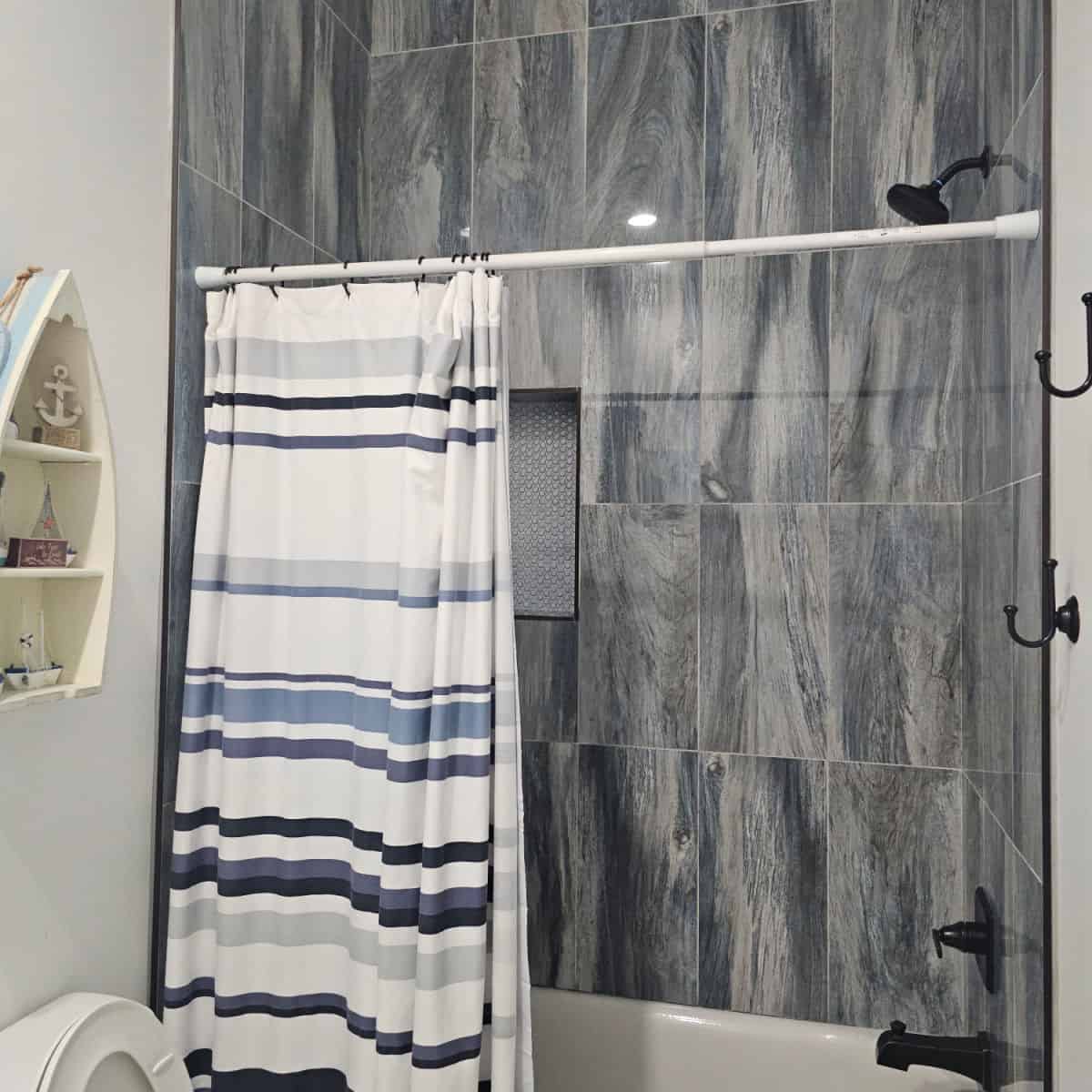 bathroom with grey slate tiles, white and blue striped shower curtain, boat shaped shelf with nautical pieces on it