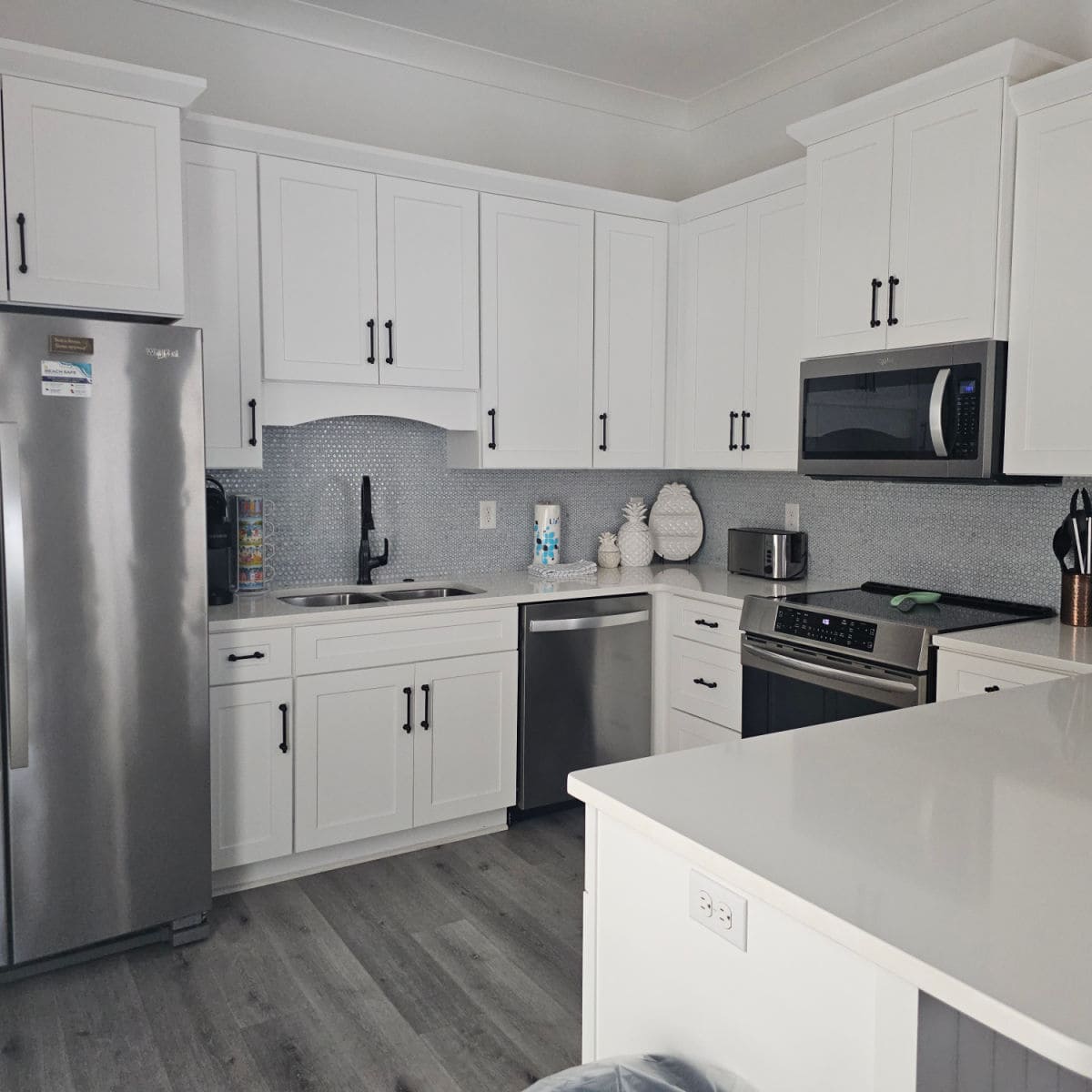 kitchen with white cabinets, grey backsplash, and stainless steel appliances.