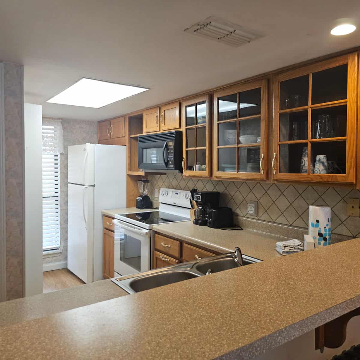 looking over a kitchen counter to brown cabinets, coffee maker and toaster, stove and refrigerator with a tile back splash