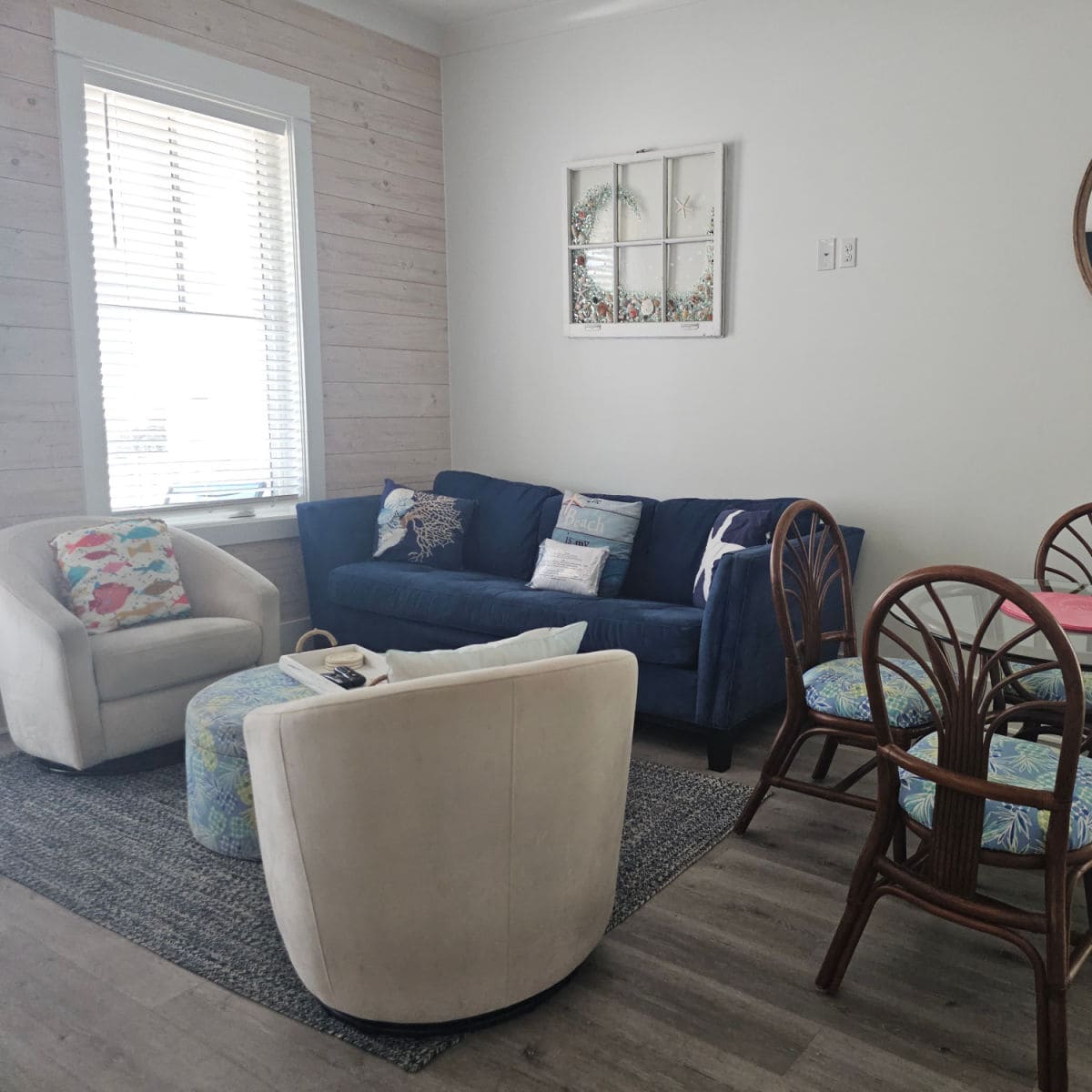 living room with blue couch, swivel chairs, next to a dining room table, shell art on the wall