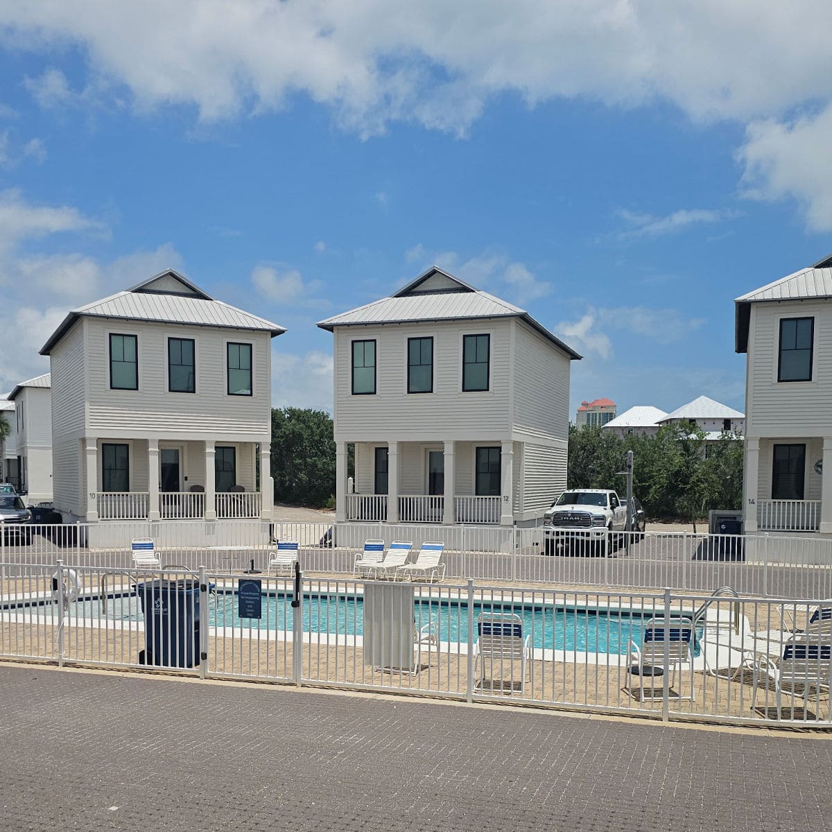 three cotttages in a row with a gated pool in front of them, lawn chairs around the pool