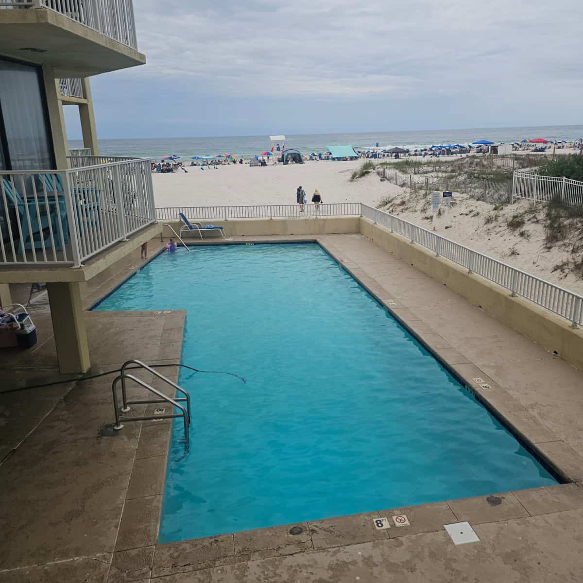 Looking over an outdoor pool with a couple of balconies to the side of it, then the beach and Gulf waters