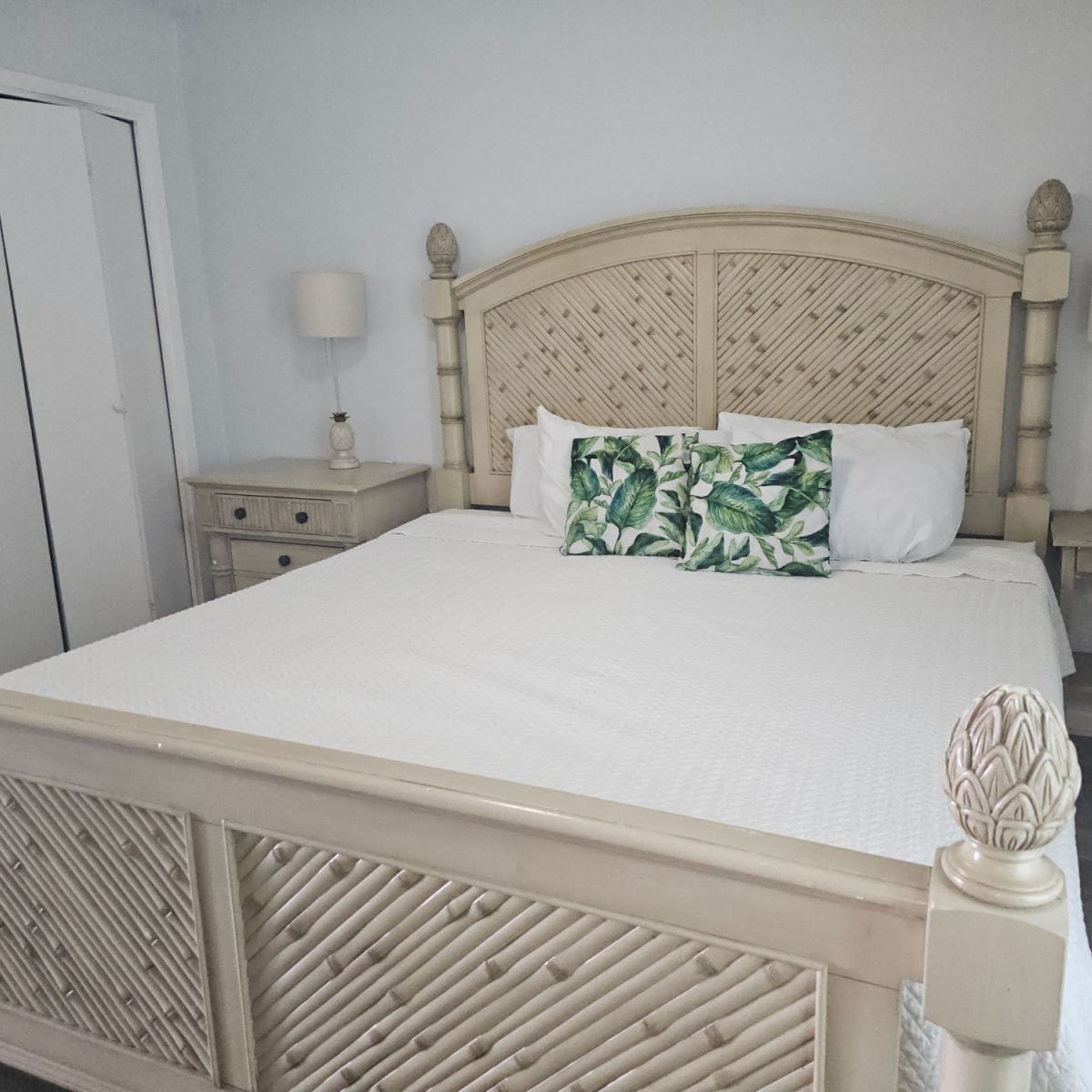 Beroom with a wooden bedframe, white linens, two palm tree covered pillows
