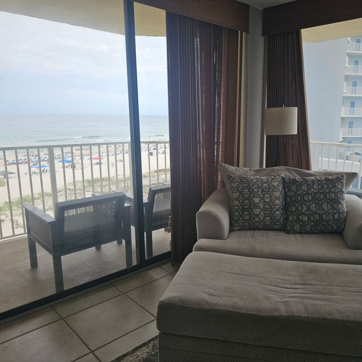 Comfy chair with two pillows next to a corner window looking out to the balcony with chairs and the beach