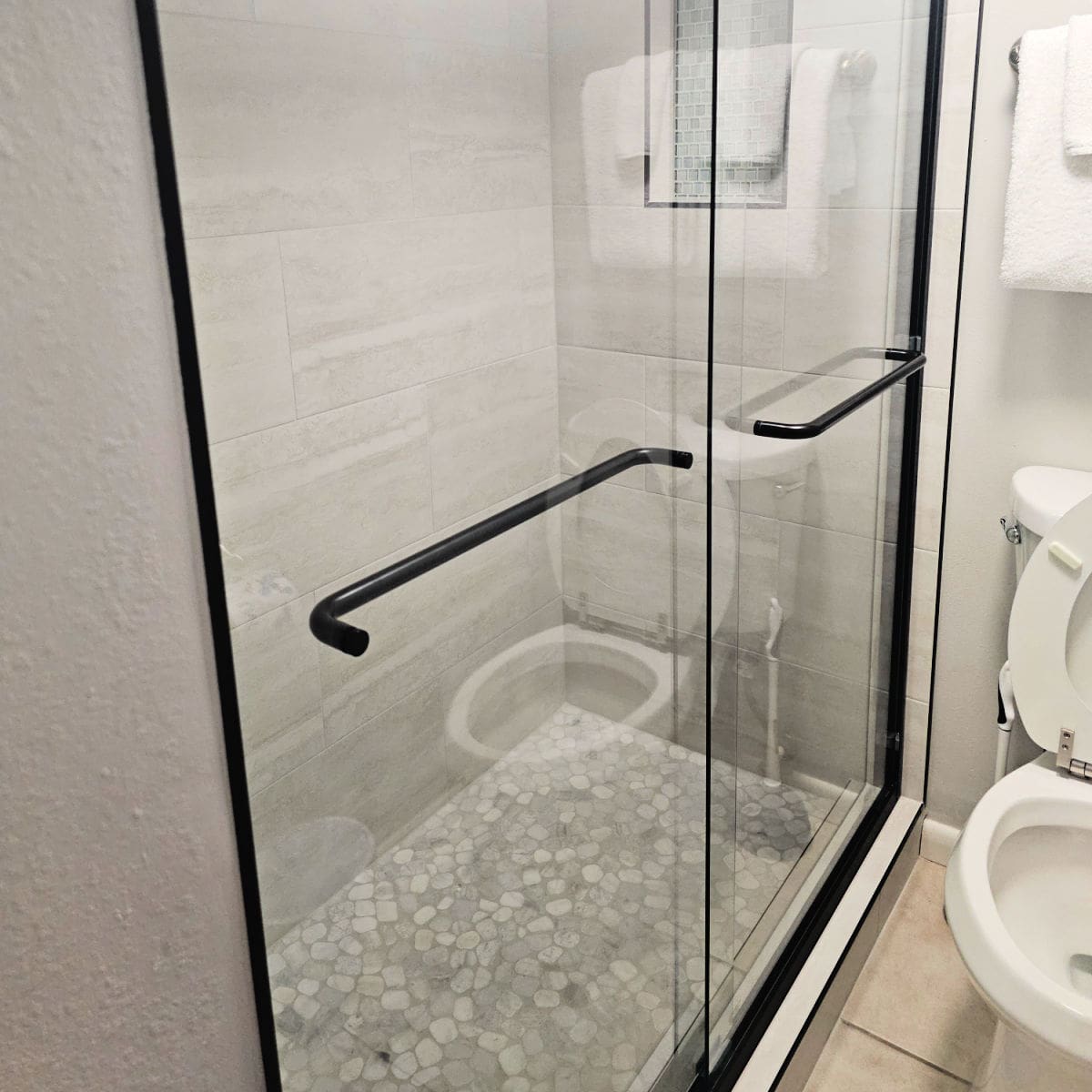Walk in shower with towels hanging over the toilet next to the shower entrance