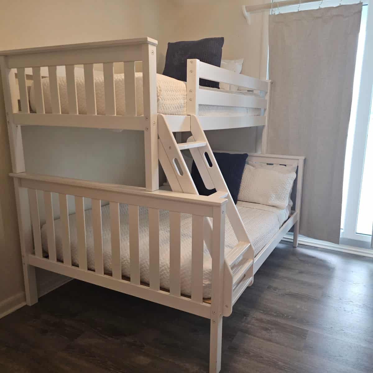 white bunkbeds with white linens, dark pillow