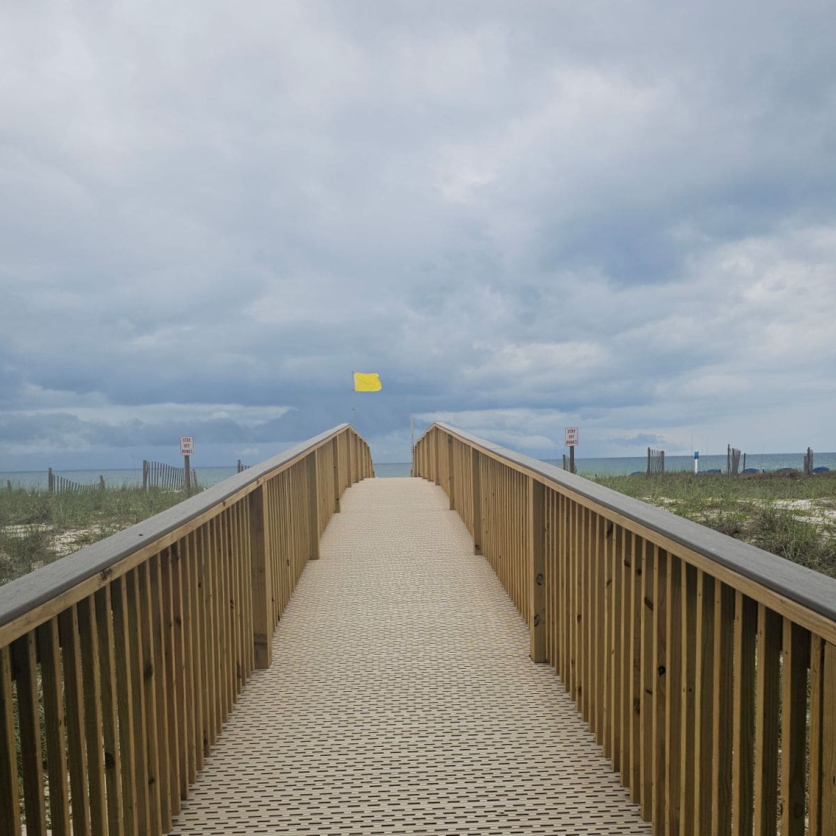 wooden walkway over and dunes with a yellow flag in the distance