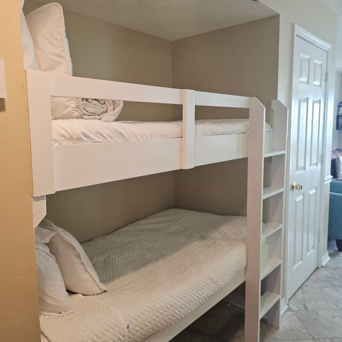 white bunkbeds built into a hallway with a white door near them.