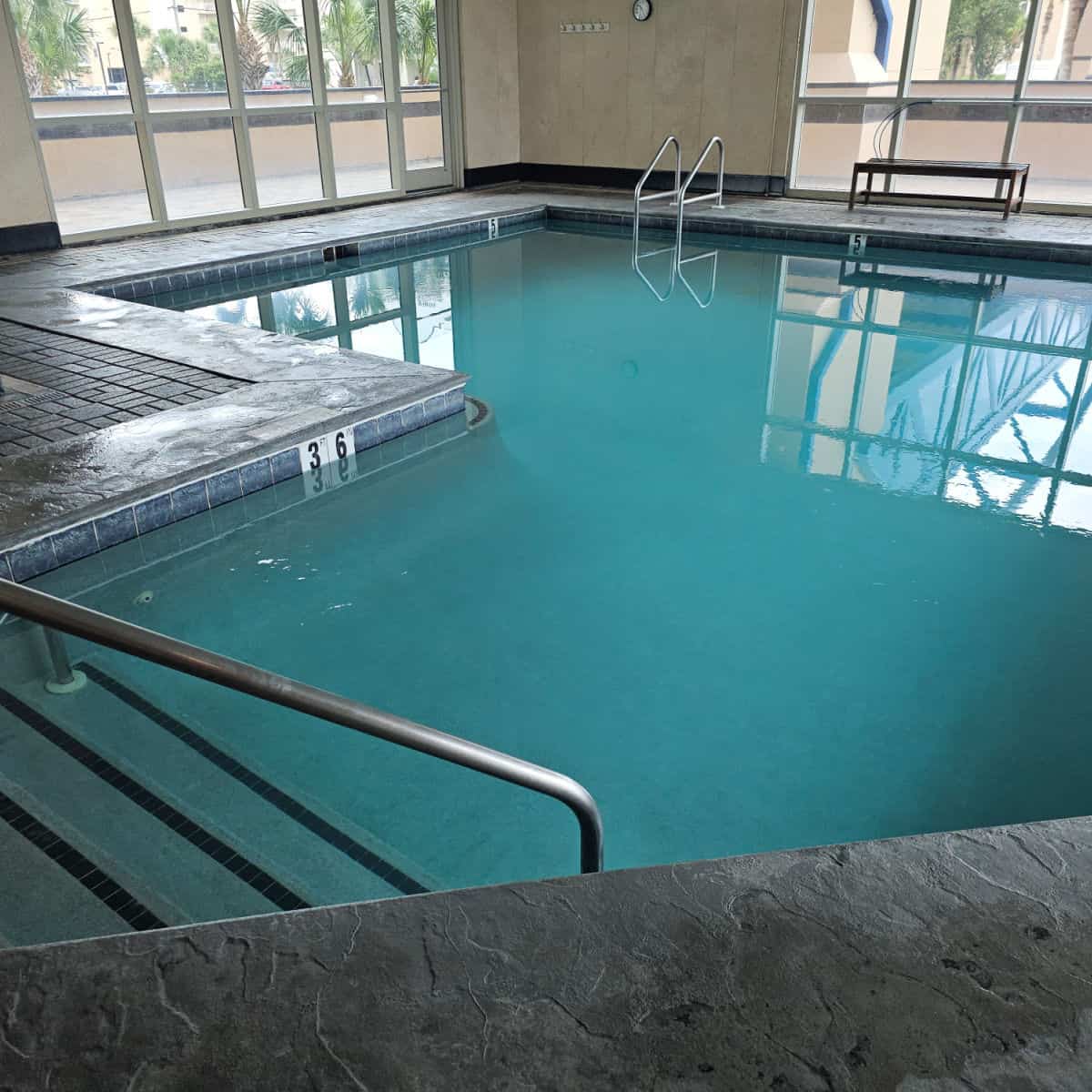 indoor pool with stairs down into th epool, bench on the far end by the glass wall