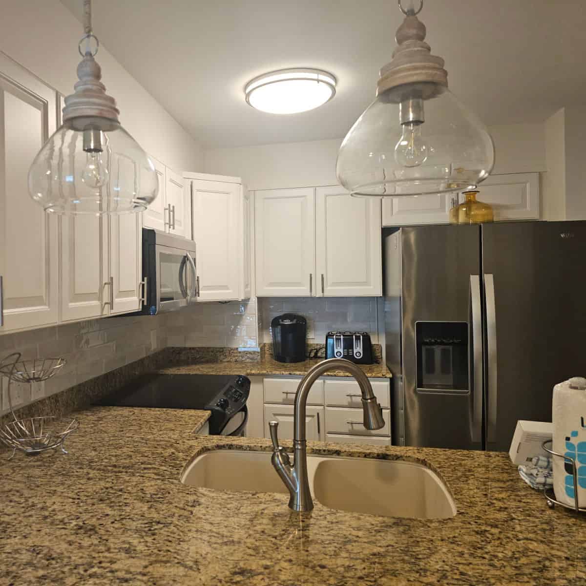 kitchen with glass lamps hanging over the counter, stainless steel appliances, and white cabinets