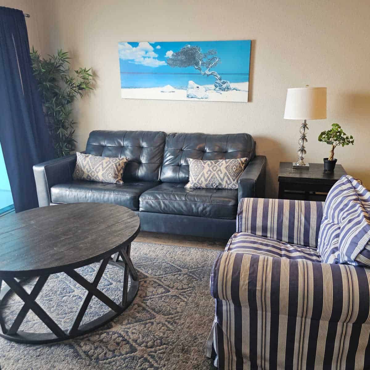 living room area with blue leather couch and white and blue striped chair next to a wooden table