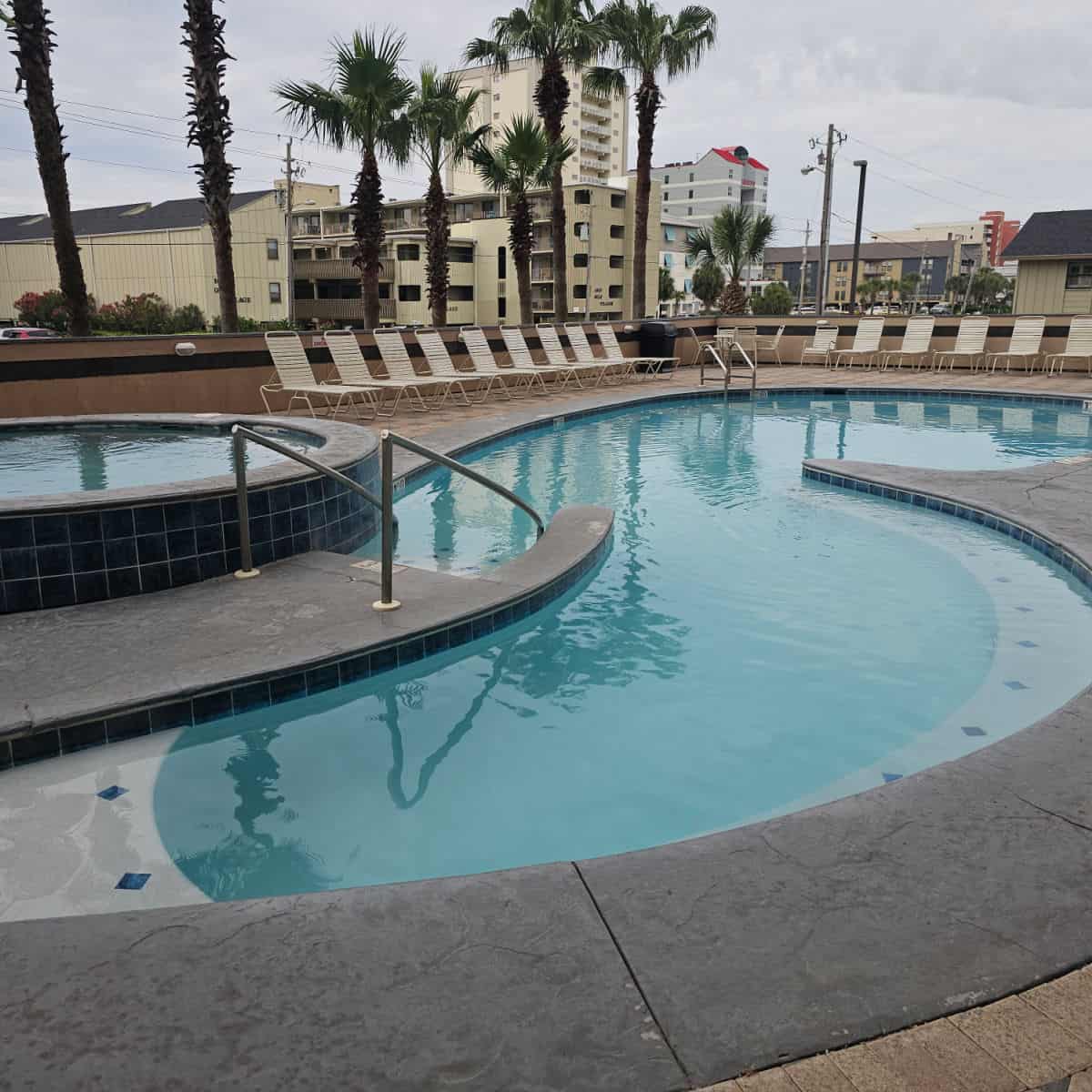 curvy outdoor pool with hot tub next to it and lounge chairs around the edges