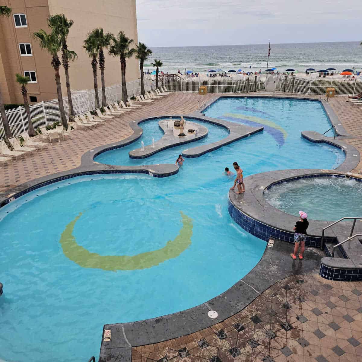 large outdoor pool with a hot tub on one side and mini lazy river on the left, looking out to the beach