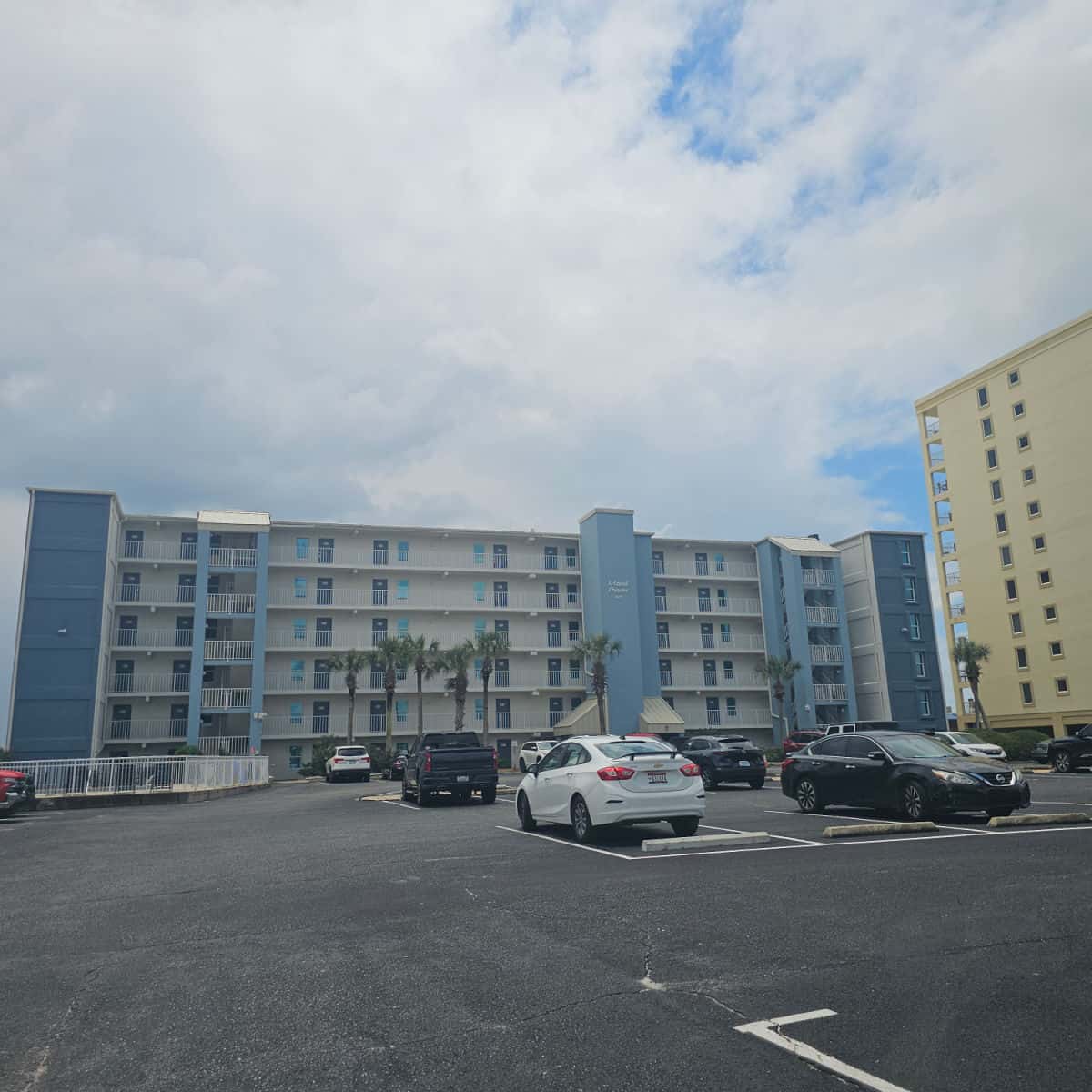 Island Shores blue and white building exterior across the parking lot with cars parked