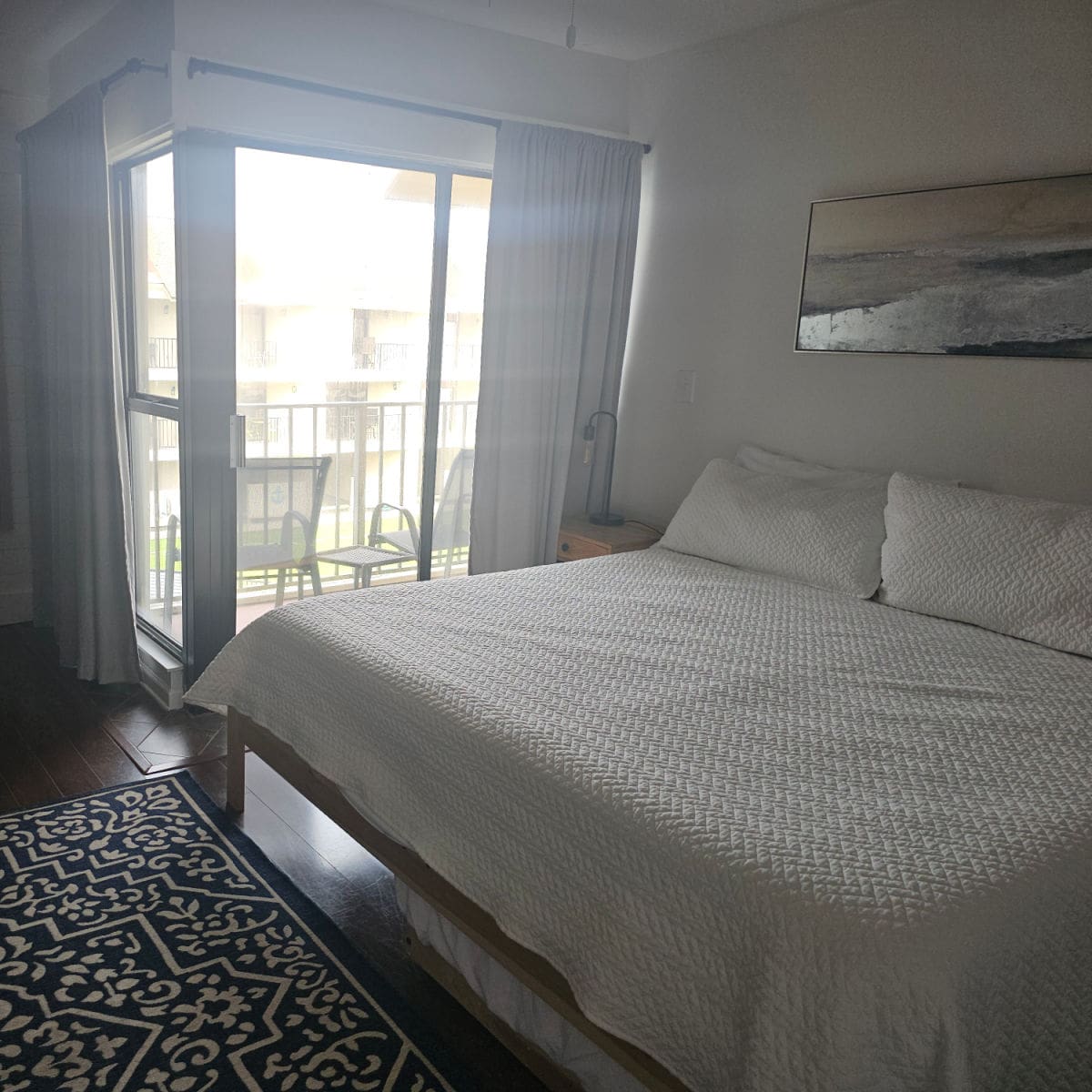 bed with white linens, art over the wall glass door to balcony
