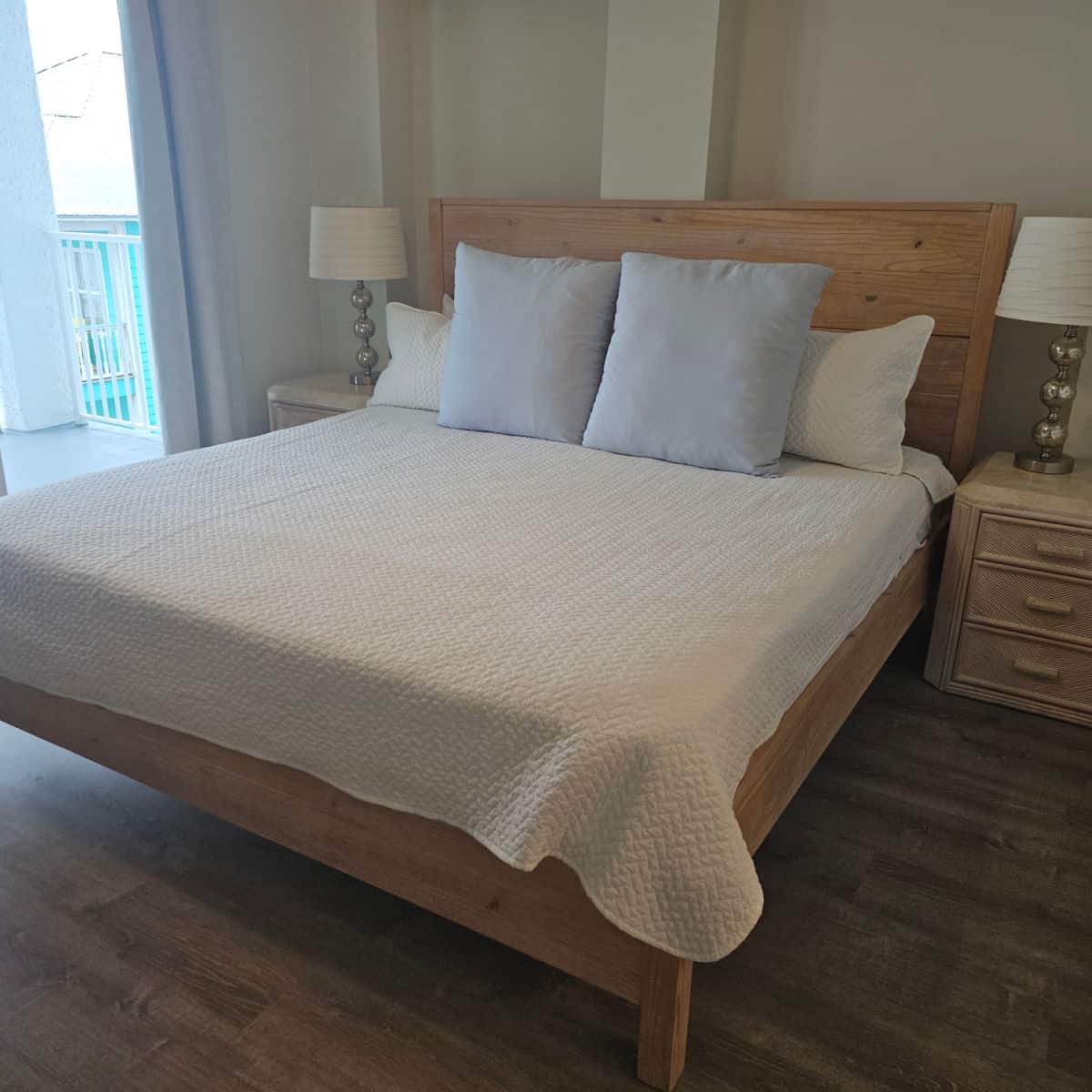 bedroom with wooden bed frame, white linens, and square pillows, lamps on nightstands