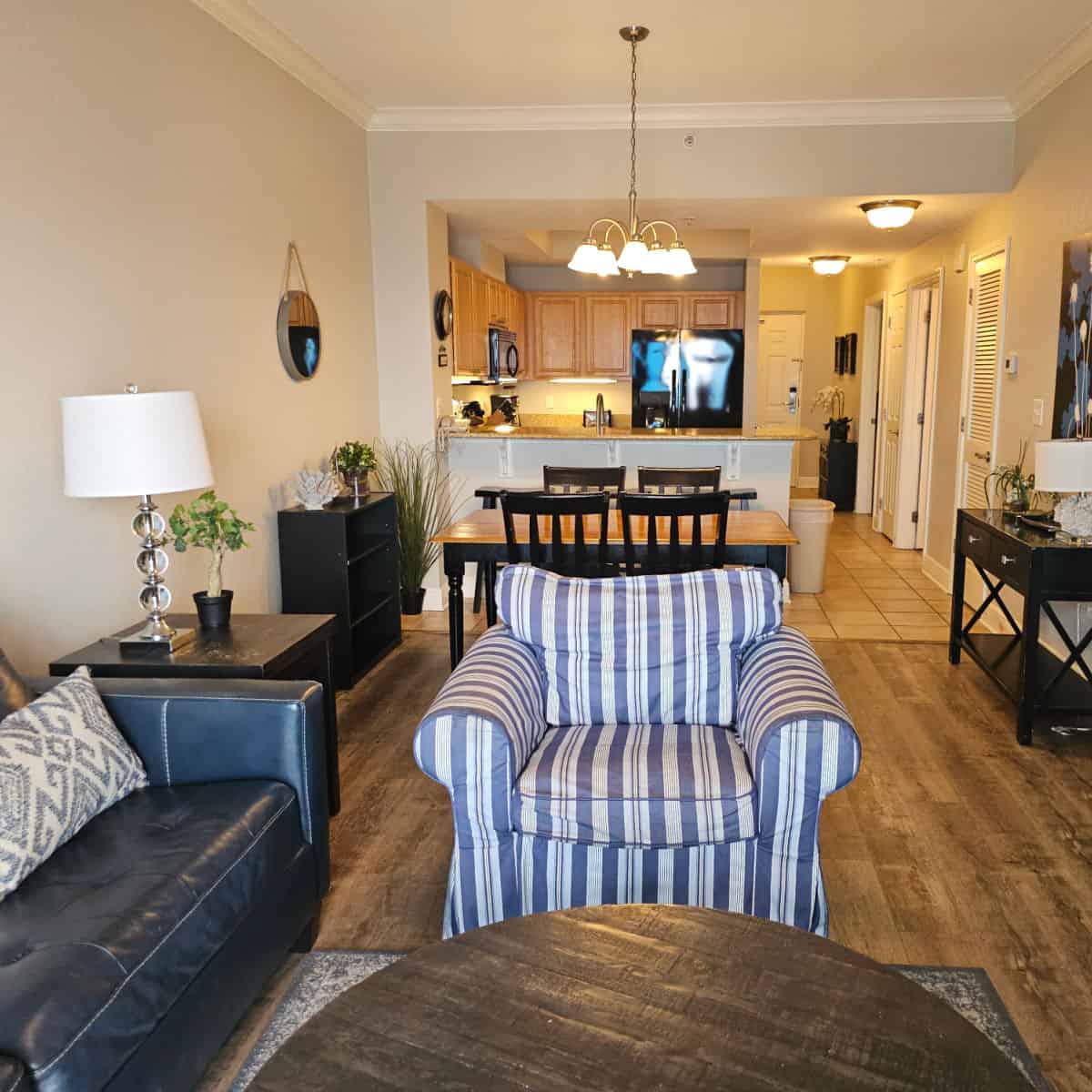 living room with blue leather couch and striped chair with a dining room table and then a kitchen