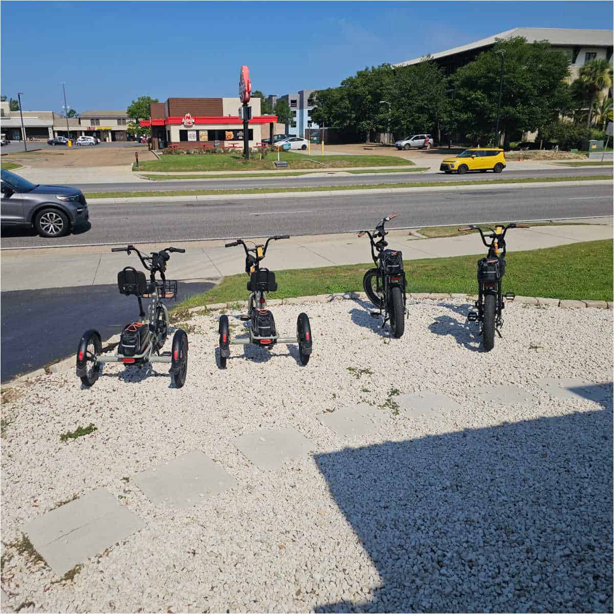 two trikes and two e-bikes on a gravel area in front of hwy 59 with an arbys across the street