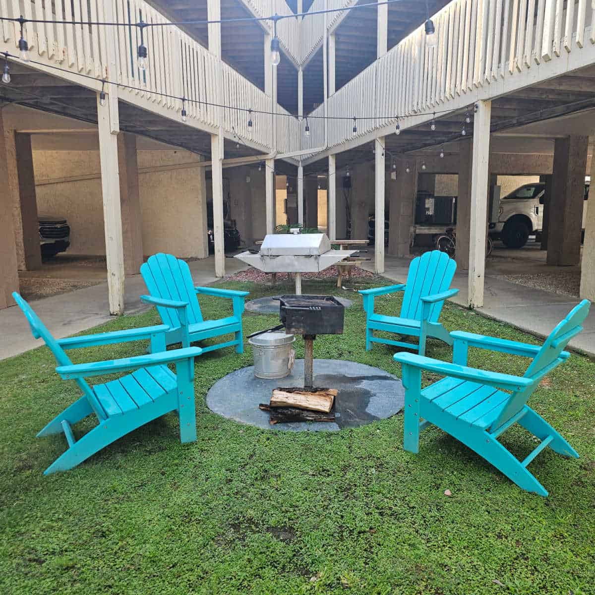 BBQ area with Adirondack chair around a charcoal grill and another grill behind it. Triangle tip of building shaped around the area