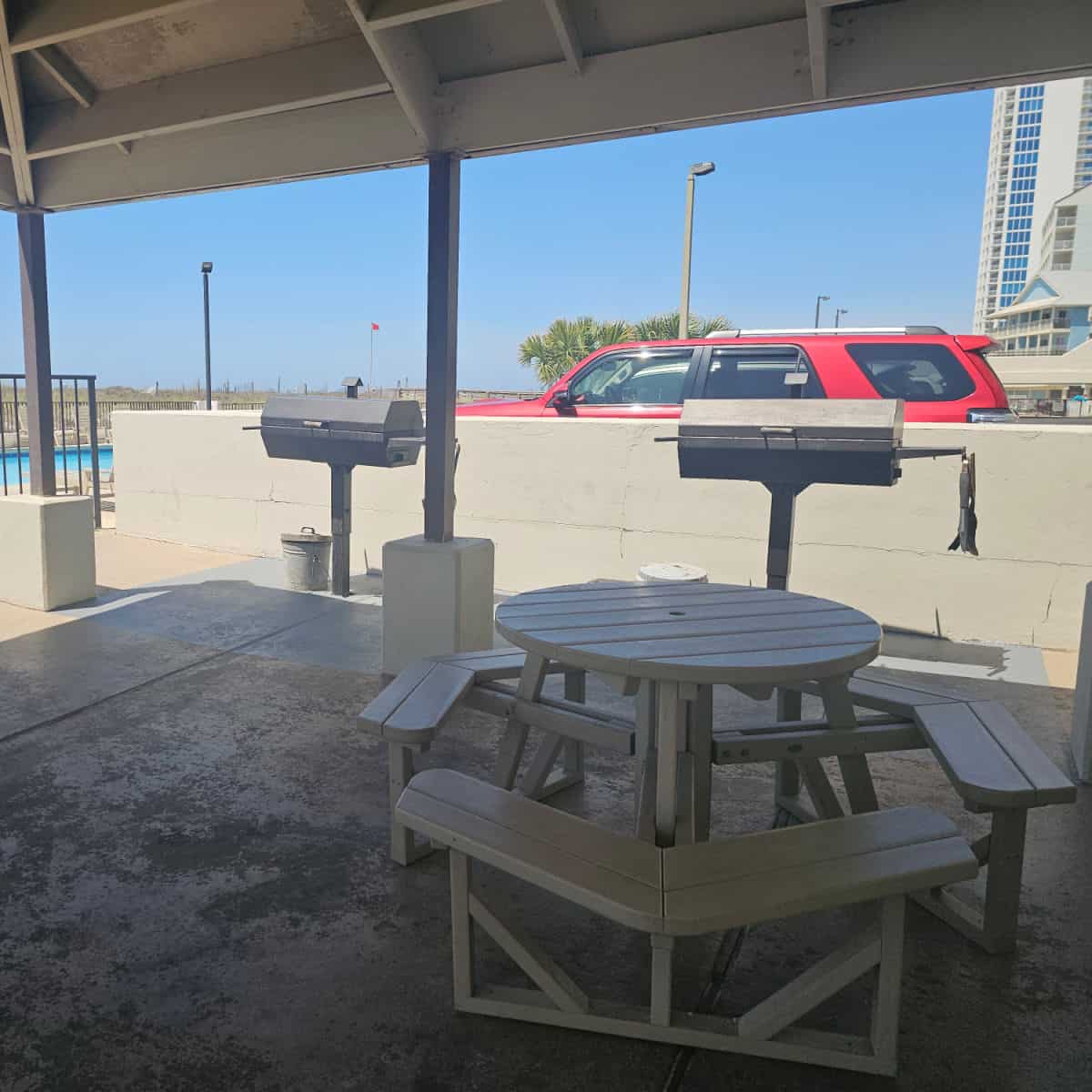 covered area with a picnic table, two charcoal grills right near it with the pool seen in the left corner
