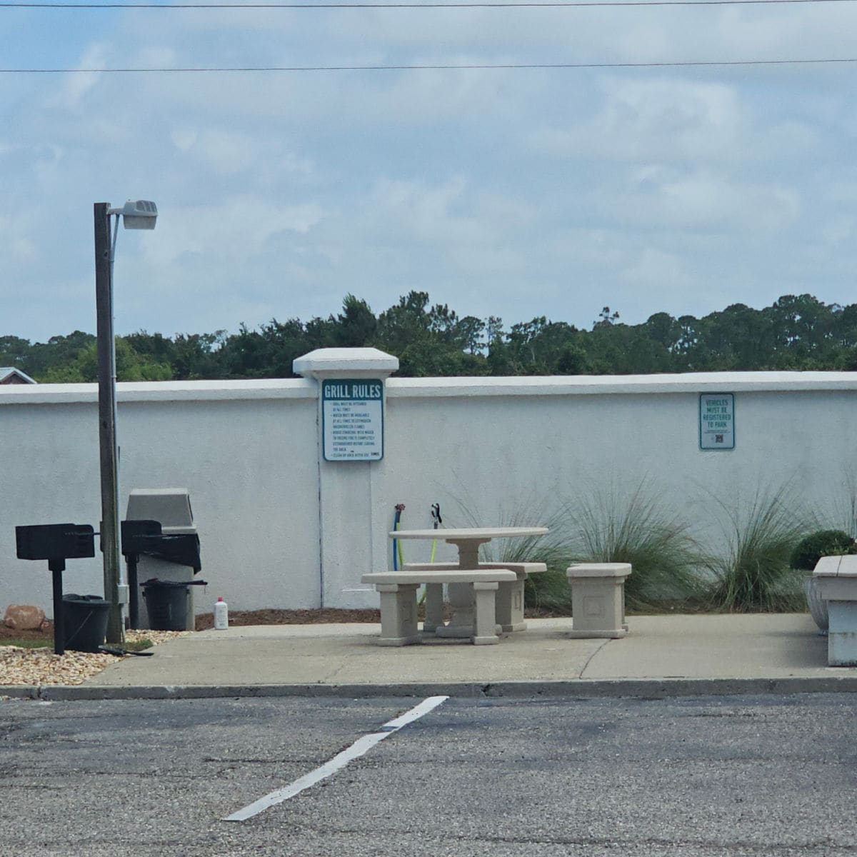 barbecue area with two charcoal grills, a table and benches, plus grill rules sign on a white wall