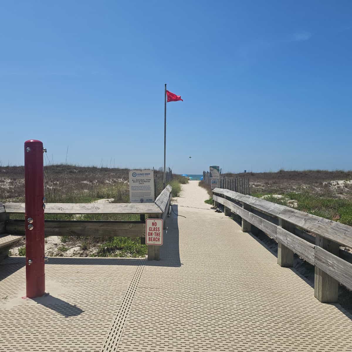 Outdoor shower on a walkway to the beach with sand and Gulf waters in the distance, red flag flying