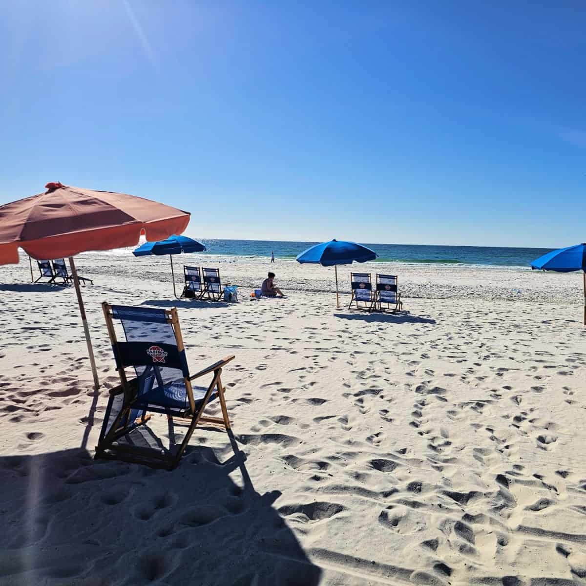Beach chairs on the beach with blue umbrellas and the Gulf waters