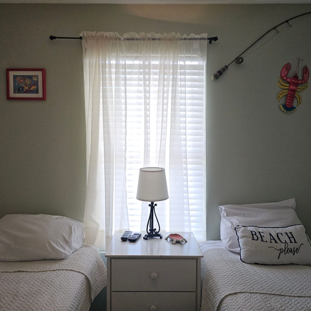 Bedroom with twin beds with a nightstand in between the beds, lobster and fishing pole on the wall