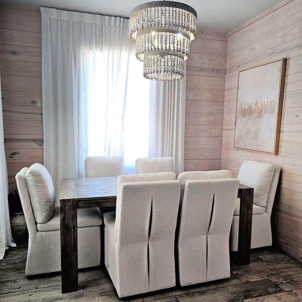 Dining room area with white chairs around a wooden table, ornate chandelier hanging over the table