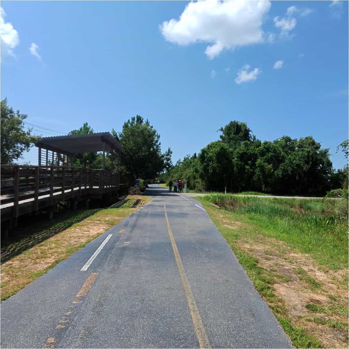 paved trail with bikers on the trail, wooden path along the side of the trail