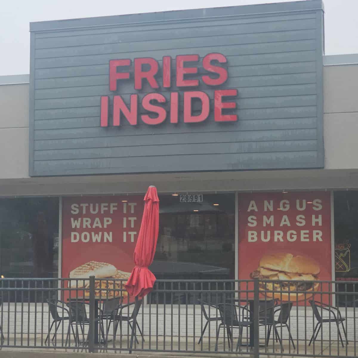 Fries Inside restaurant exterior with Stuff it wrap it down it sign and angus smash burger sign, tables and chairs outside