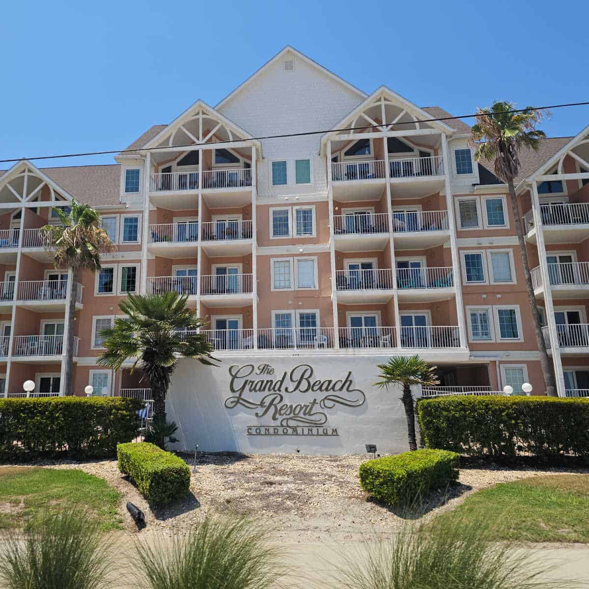The Grand Beach Resort Condominium sign in front of a pink and white multi-story building